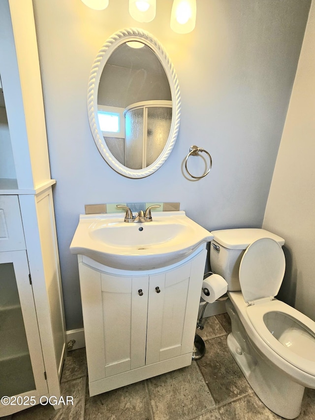 bathroom featuring toilet, vanity, a shower with shower door, and baseboards