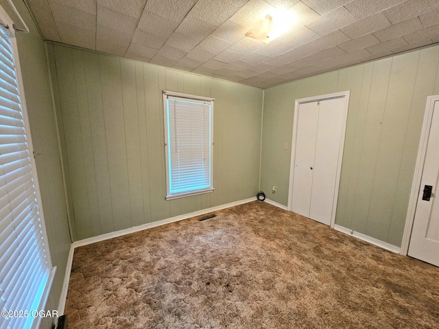 unfurnished bedroom with carpet flooring, wood walls, and baseboards