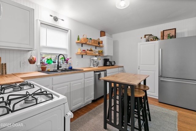 kitchen featuring appliances with stainless steel finishes, wooden counters, a sink, white cabinets, and wood finished floors