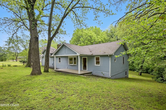 back of house with a lawn, a wooden deck, roof with shingles, and a chimney