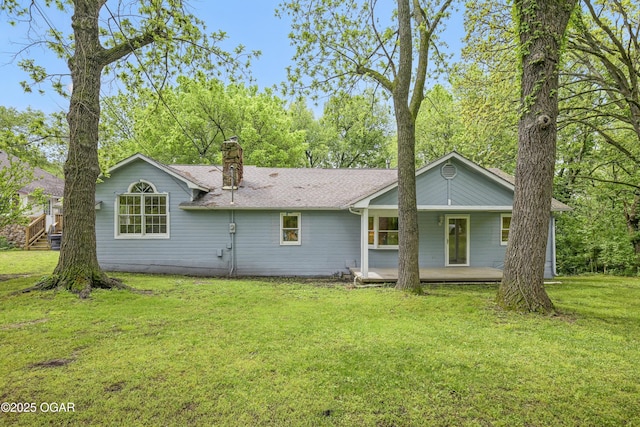 rear view of house featuring a chimney, a lawn, roof with shingles, and covered porch