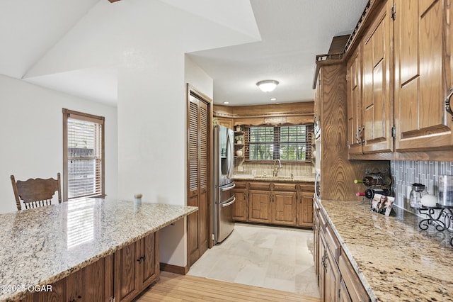 kitchen featuring tasteful backsplash, plenty of natural light, stainless steel refrigerator with ice dispenser, and light stone countertops