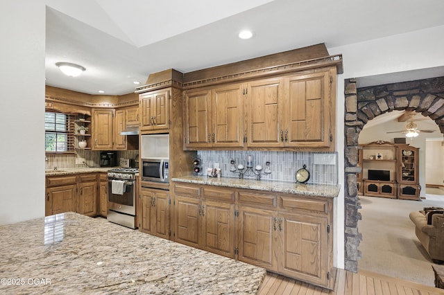 kitchen featuring stainless steel appliances, open shelves, ceiling fan, backsplash, and light stone counters