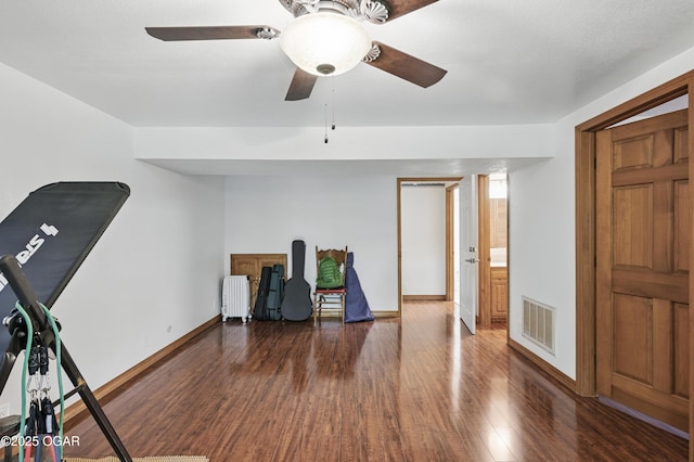 exercise room with radiator, wood finished floors, a ceiling fan, and baseboards