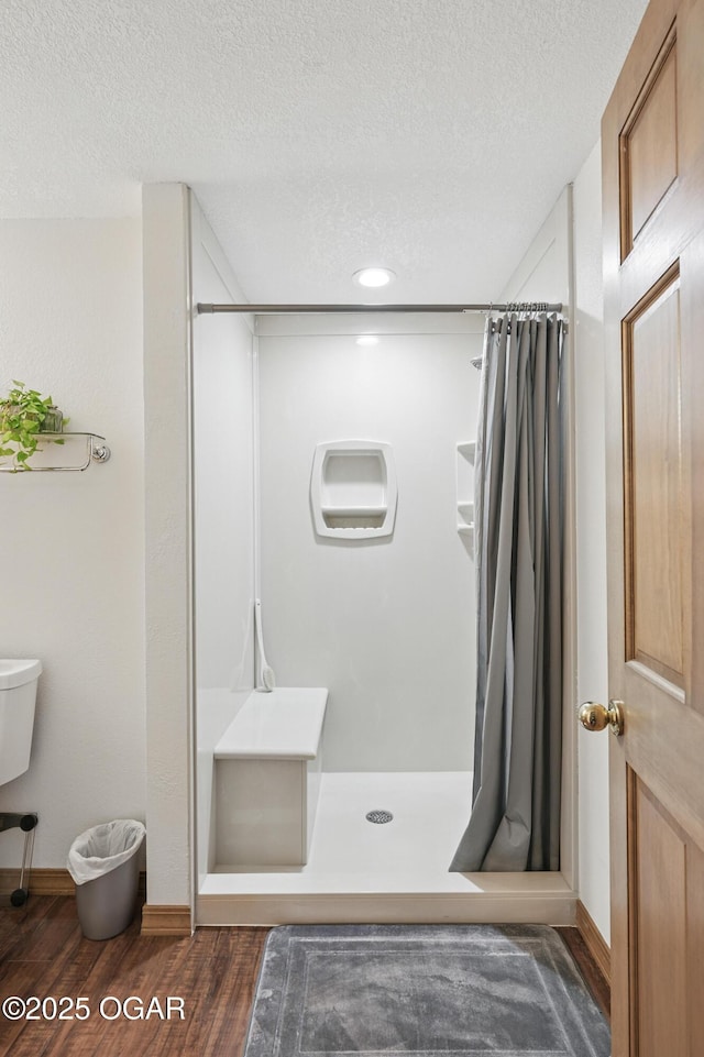 full bath featuring a stall shower, wood finished floors, a textured ceiling, baseboards, and recessed lighting