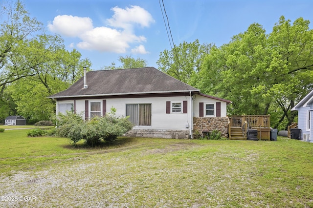 back of property featuring a wooden deck, a yard, stone siding, and a shingled roof