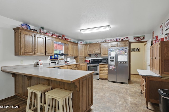 kitchen with appliances with stainless steel finishes, a peninsula, a kitchen bar, and light countertops