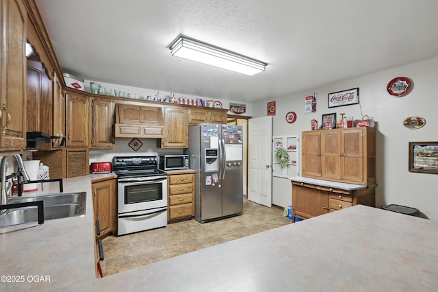 kitchen with appliances with stainless steel finishes, a sink, light countertops, and brown cabinets