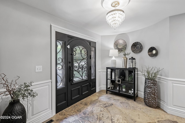 entryway with stone flooring, a decorative wall, a chandelier, and a wainscoted wall