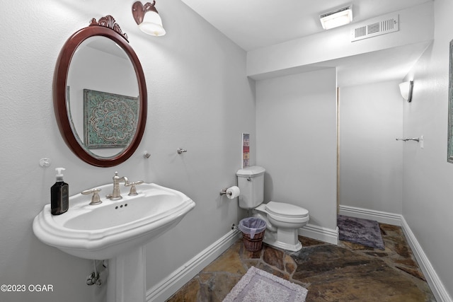 bathroom with toilet, stone finish floors, and baseboards