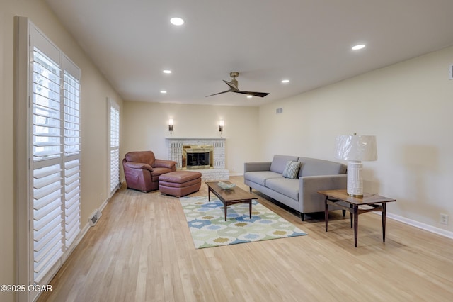 living room featuring a ceiling fan, baseboards, light wood-style floors, recessed lighting, and a glass covered fireplace
