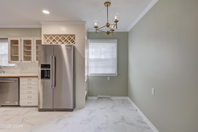 kitchen featuring stainless steel appliances, light marble finish flooring, crown molding, glass insert cabinets, and a chandelier