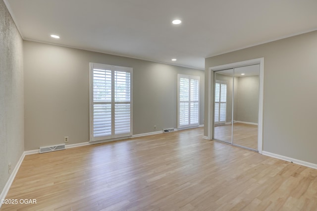 unfurnished bedroom featuring multiple windows, light wood finished floors, baseboards, recessed lighting, and ornamental molding