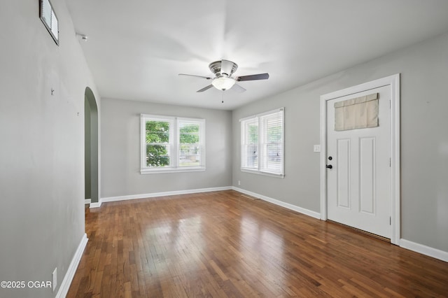 unfurnished room with ceiling fan, arched walkways, wood-type flooring, and baseboards