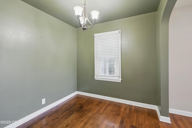 spare room with arched walkways, baseboards, a chandelier, and dark wood finished floors