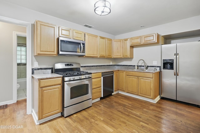 kitchen with appliances with stainless steel finishes, a sink, light brown cabinetry, and light wood-type flooring