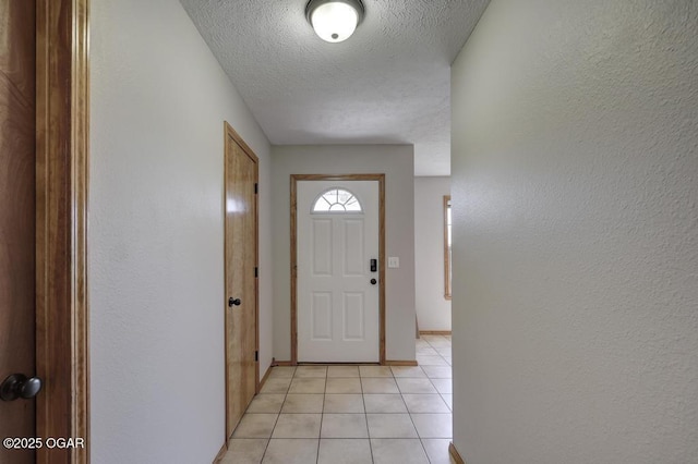 doorway to outside with a textured ceiling, light tile patterned floors, and baseboards