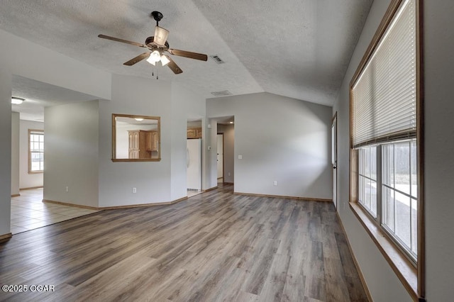 unfurnished living room with lofted ceiling, ceiling fan, light wood-style flooring, a textured ceiling, and baseboards