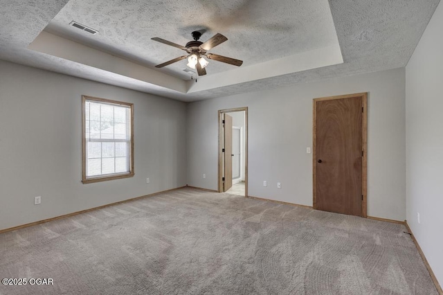 empty room featuring a tray ceiling, a textured ceiling, ceiling fan, baseboards, and light colored carpet