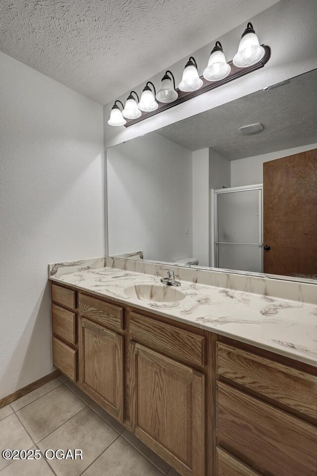 bathroom featuring a shower stall, vanity, tile patterned flooring, baseboards, and a textured ceiling