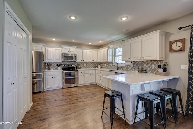 kitchen featuring appliances with stainless steel finishes, a sink, a peninsula, white cabinetry, and recessed lighting
