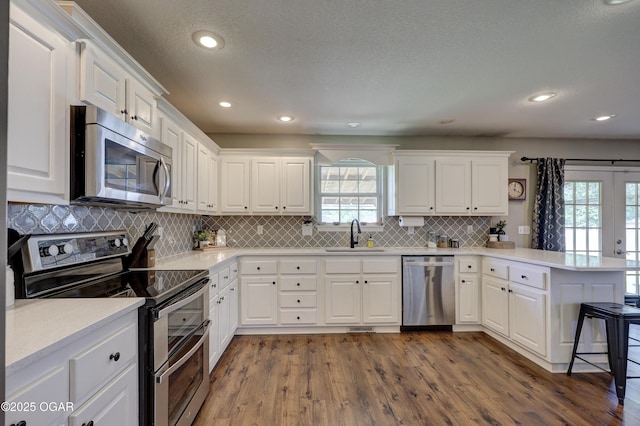 kitchen with appliances with stainless steel finishes, a peninsula, a sink, dark wood finished floors, and recessed lighting