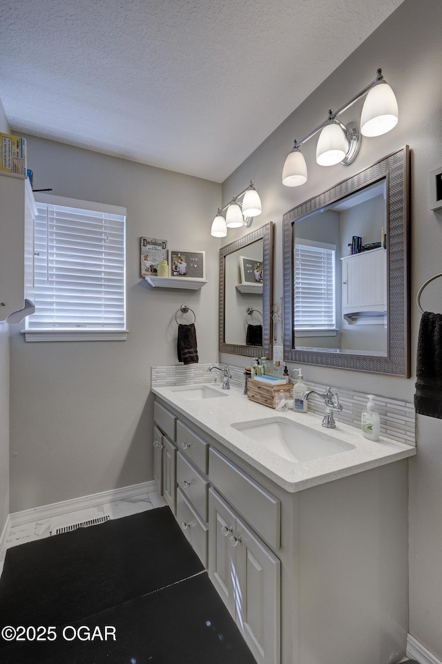 full bath with baseboards, double vanity, and a textured ceiling