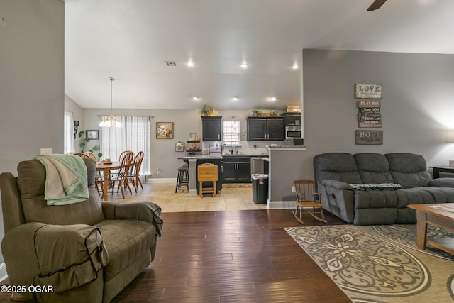 living room with a chandelier, light wood finished floors, a ceiling fan, baseboards, and lofted ceiling