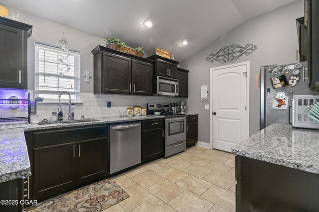 kitchen featuring appliances with stainless steel finishes, a sink, vaulted ceiling, backsplash, and dark cabinetry