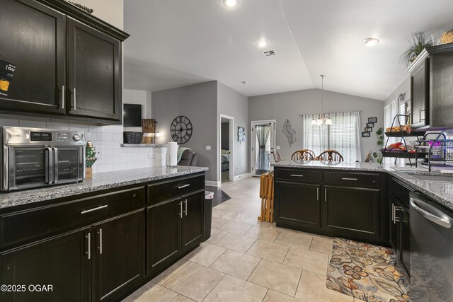 kitchen featuring dishwasher, a peninsula, vaulted ceiling, tasteful backsplash, and light stone countertops
