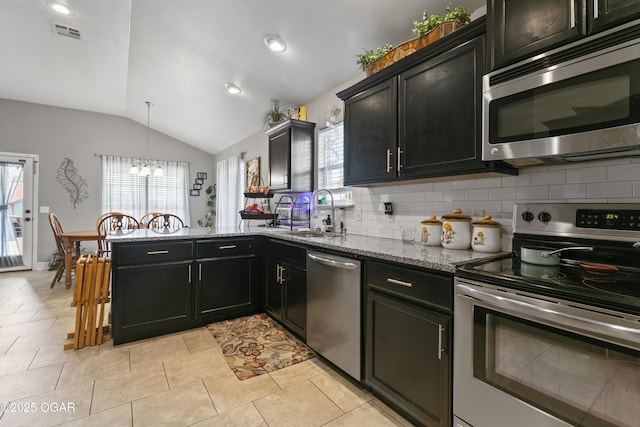 kitchen with stainless steel appliances, a sink, vaulted ceiling, a peninsula, and plenty of natural light