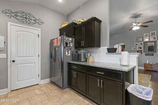 kitchen featuring stainless steel refrigerator with ice dispenser, a ceiling fan, decorative backsplash, light stone counters, and baseboards