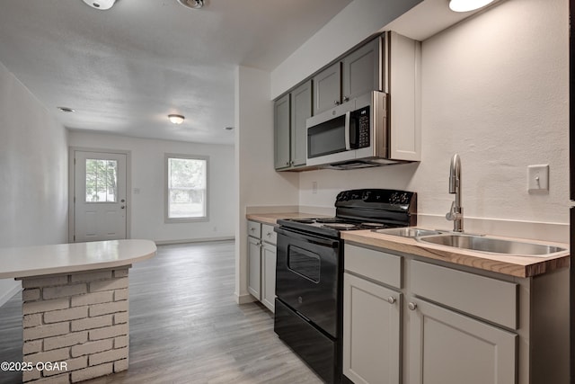 238 E 21st St, Baxter Springs, KS 66713 - kitchen with stainless steel microwave, black electric range, a sink, light wood-style flooring, and light countertops