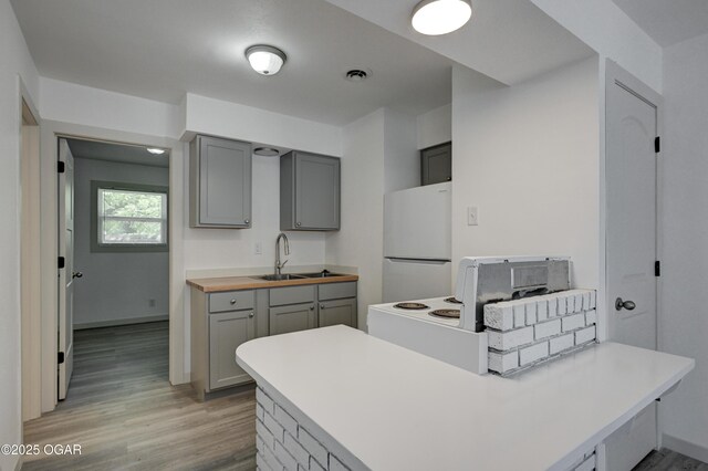238 E 21st St, Baxter Springs, KS 66713 - kitchen with freestanding refrigerator, gray cabinetry, a sink, a peninsula, and light wood-style floors