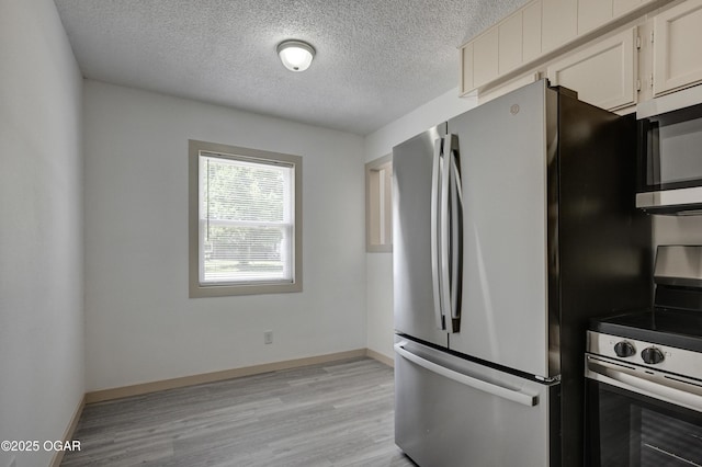 238 E 21st St, Baxter Springs, KS 66713 - kitchen featuring appliances with stainless steel finishes, a textured ceiling, light wood-style flooring, baseboards, and white cabinets