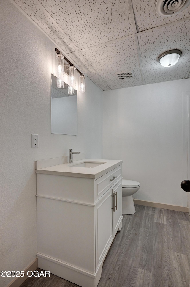 238 E 21st St, Baxter Springs, KS 66713 - bathroom with wood finished floors, a paneled ceiling, vanity, baseboards, and toilet