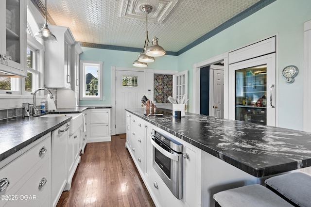 kitchen featuring oven, dark countertops, a sink, white cabinets, and a breakfast bar area