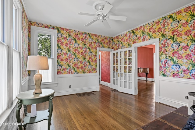 sitting room with wallpapered walls, a wainscoted wall, french doors, a ceiling fan, and healthy amount of natural light