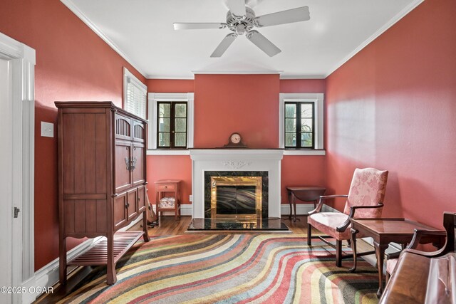 living area with wood finished floors, healthy amount of natural light, a ceiling fan, crown molding, and a fireplace with flush hearth