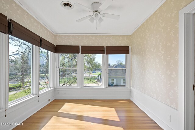 unfurnished sunroom with wood finished floors, ornamental molding, wallpapered walls, and baseboards