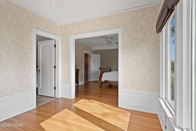 unfurnished room with a ceiling fan, light wood finished floors, and a wainscoted wall