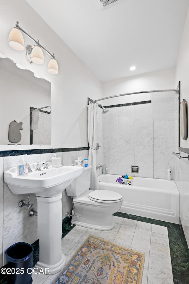full bath with toilet, shower / tub combo with curtain, tile walls, and wainscoting