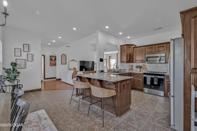 kitchen with stainless steel appliances, a breakfast bar, a sink, open floor plan, and a peninsula