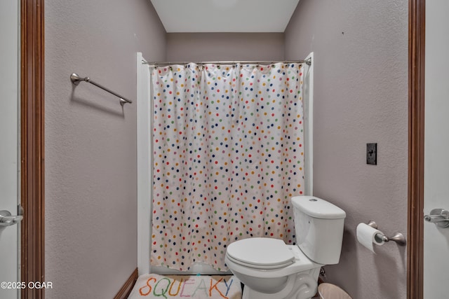 full bath featuring a shower with curtain, toilet, and a textured wall