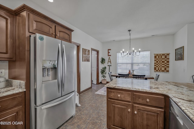 kitchen with stainless steel appliances, a chandelier, pendant lighting, light stone countertops, and dark tile patterned flooring