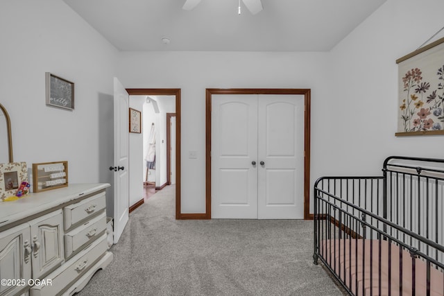 bedroom featuring light colored carpet, a crib, a closet, a ceiling fan, and baseboards