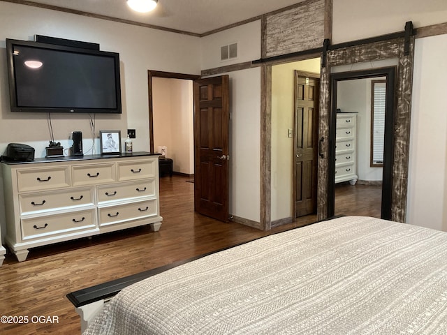 bedroom with dark wood finished floors, crown molding, baseboards, and a barn door