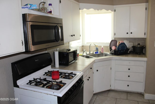 504 E Jackson St, Pittsburg, KS 66762 - kitchen with stainless steel microwave, gas range, a sink, white cabinets, and light tile patterned floors