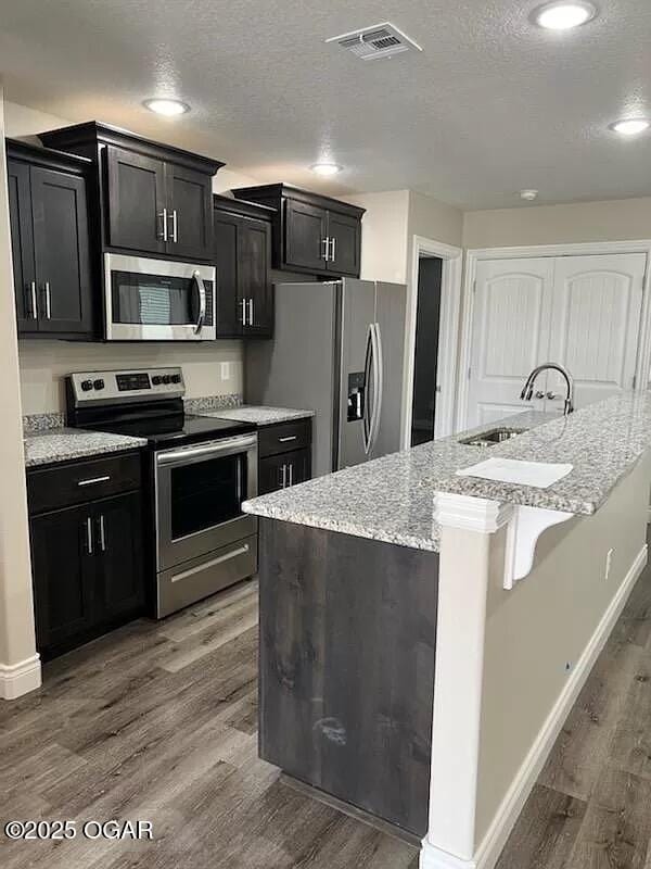 1403 E Valley St, Joplin, MO 64801 - kitchen with stainless steel appliances, a sink, a textured ceiling, baseboards, and dark cabinetry