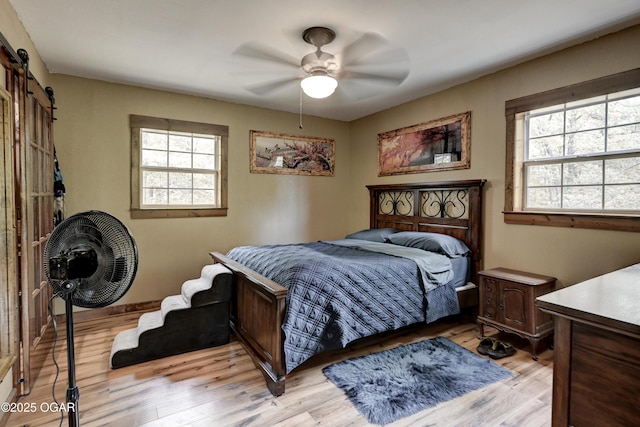 22351 S 672nd Rd, Wyandotte, OK 74370 - bedroom with multiple windows, light wood-style floors, a barn door, and ceiling fan